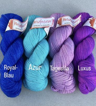Das Bild zeigt vier Stränge handgefärbte Wolle von Herzfasern No. 11, nebeneinander gelegt. Von links nach rechts: ein kräftiges Royalblau, ein leuchtendes Azurblau, ein zartes Tageslila und ein sattes, kräftiges Violett mit dem Namen Luxus. Alle Stränge 